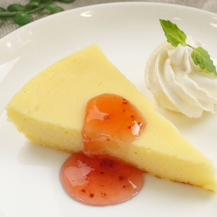 いちごジャムをかけた、白い皿に盛り付けたベイクドチーズケーキ