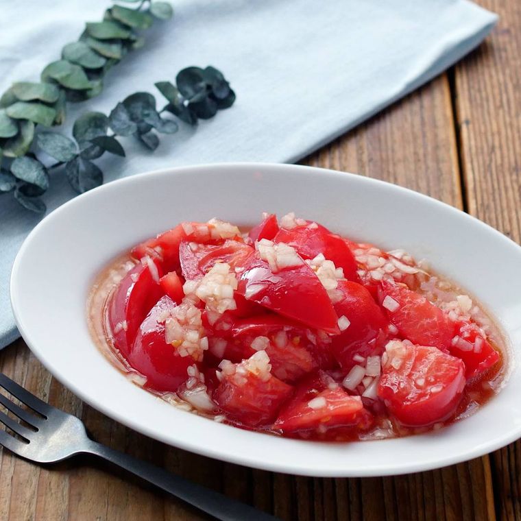 白い楕円型の皿に盛り付けた玉ねぎドレッシングがけのトマトサラダ