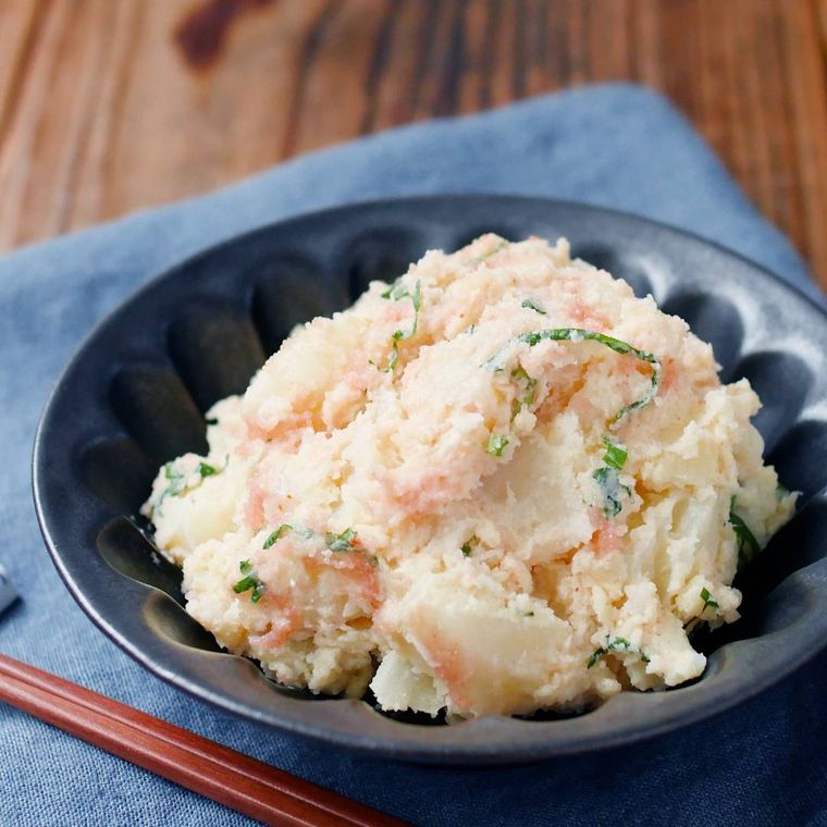 黒い丸皿にじゃがいもの明太子和えが盛られている