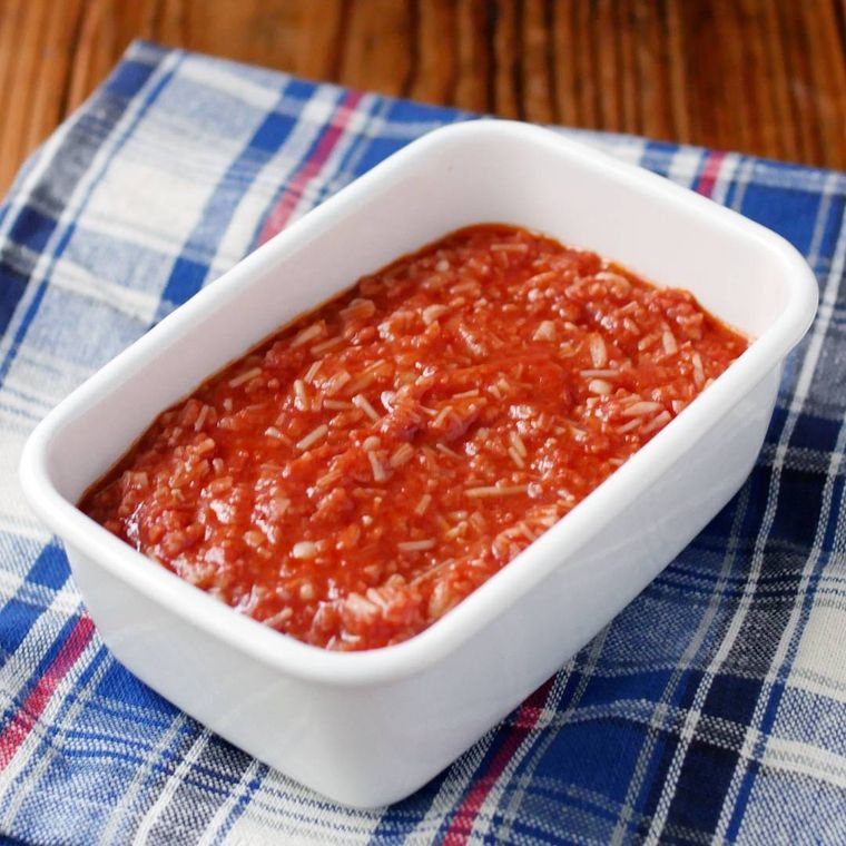 白い長方形の保存容器にえのきのミートソースが入っており、青いチェックのランチョンマットの上に置かれている