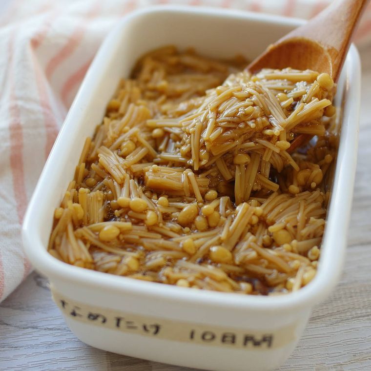 白い長方形の保存容器に自家製なめたけが入っており、木のスプーンですくっている