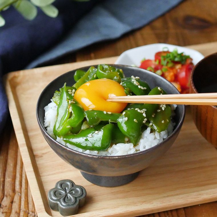 茶碗に盛られた、やみつき旨だれピーマンと卵黄をのせたごはん