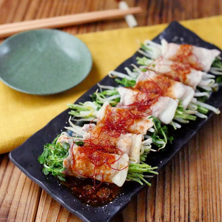 黒い長方形の皿に盛られているピリ辛もやしと豆苗の豚肉巻き