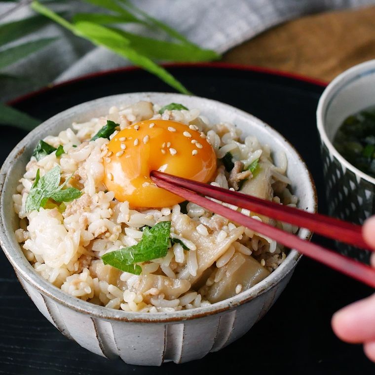 茶碗に盛られた甘辛鶏しそ混ぜごはんのトッピングの卵黄を、箸で割ろうとしている様子