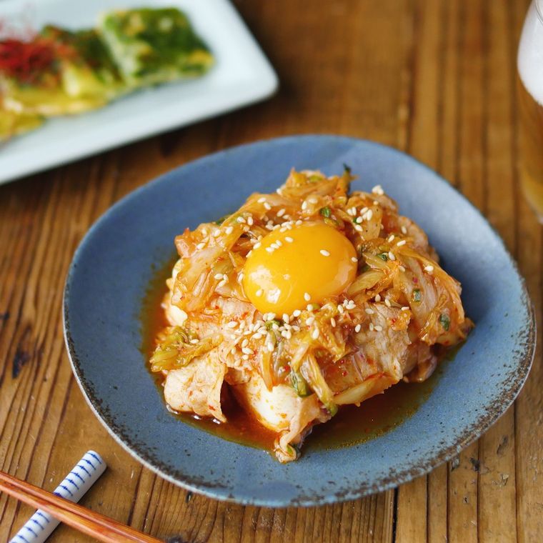 青い皿に盛られた豚肉とキムチの冷奴卵黄のせ