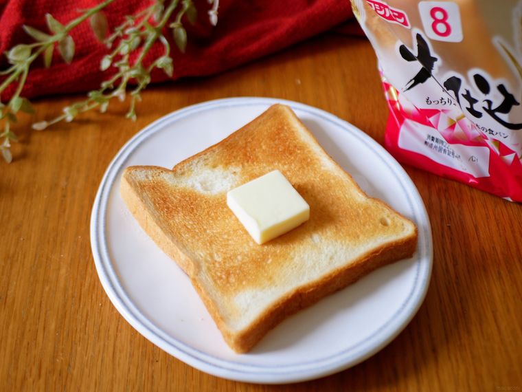 白い皿にのったバターのせトースト、奥にフジパン本仕込のパッケージが見えている様子