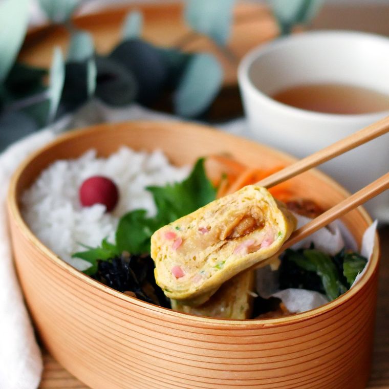 お弁当箱に入ったお好み焼き風卵焼きを、箸でつまんでいる様子