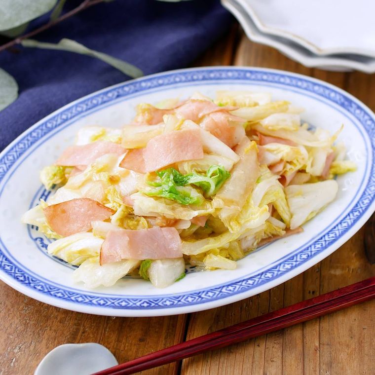 青い縁取りがある皿に盛りつけられた白菜とハムの中華風味炒め