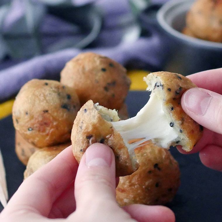 黒い皿に盛りつけられたチーズボールを手で割っている様子