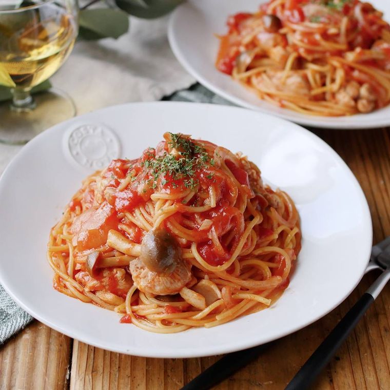 白い皿に盛りつけられた鶏もも肉としめじのトマトパスタ