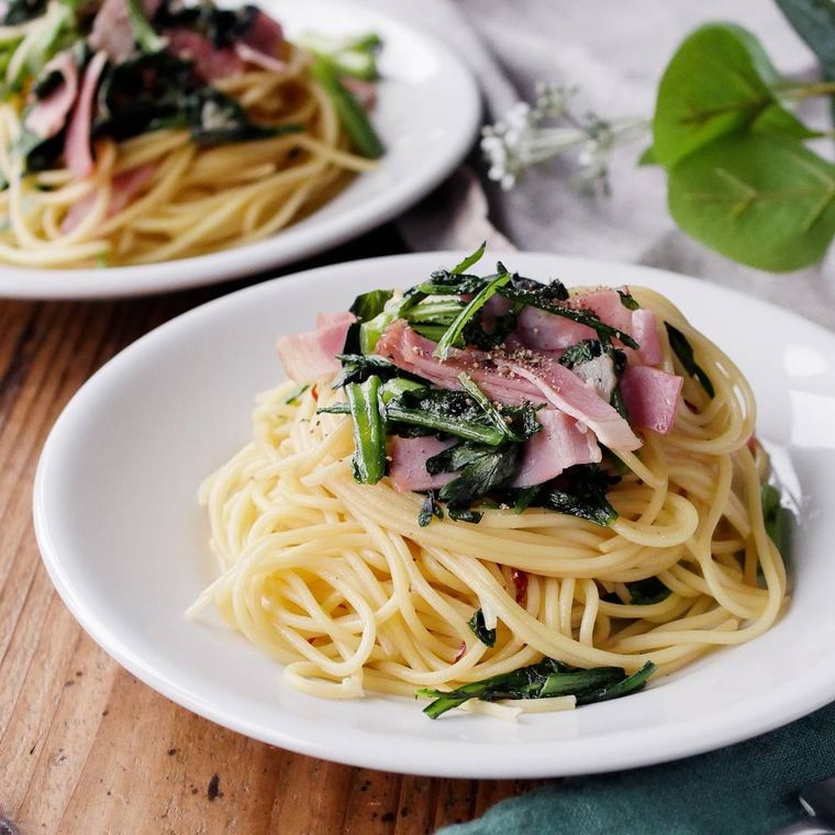 白色の丸皿に盛られた春菊とベーコンの和風ペペロンチーノ