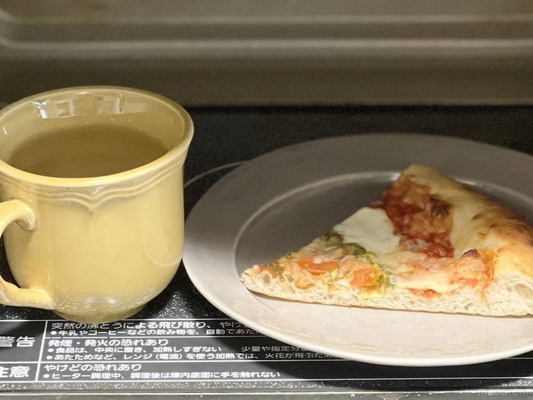 電子レンジの中にある、水を入れたコップとピザ