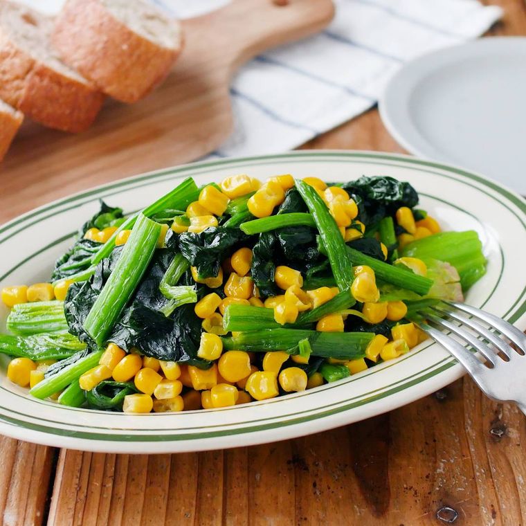 緑色の縁取りの白色の楕円の皿に盛られたほうれん草とコーンのバター炒め