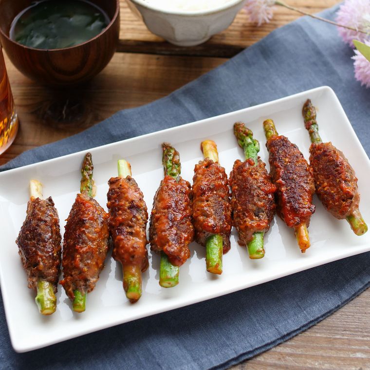 白い長皿に盛りつけられたアスパラガスのひき肉巻き焼き