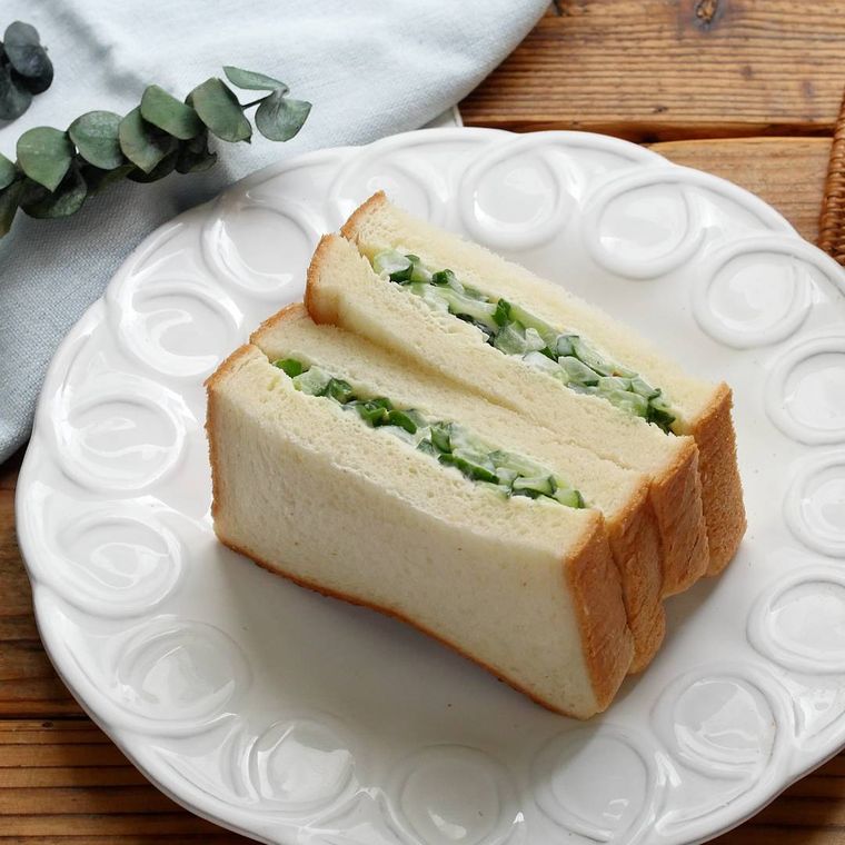 白い皿に盛りつけられている2個のきゅうりサンドイッチ