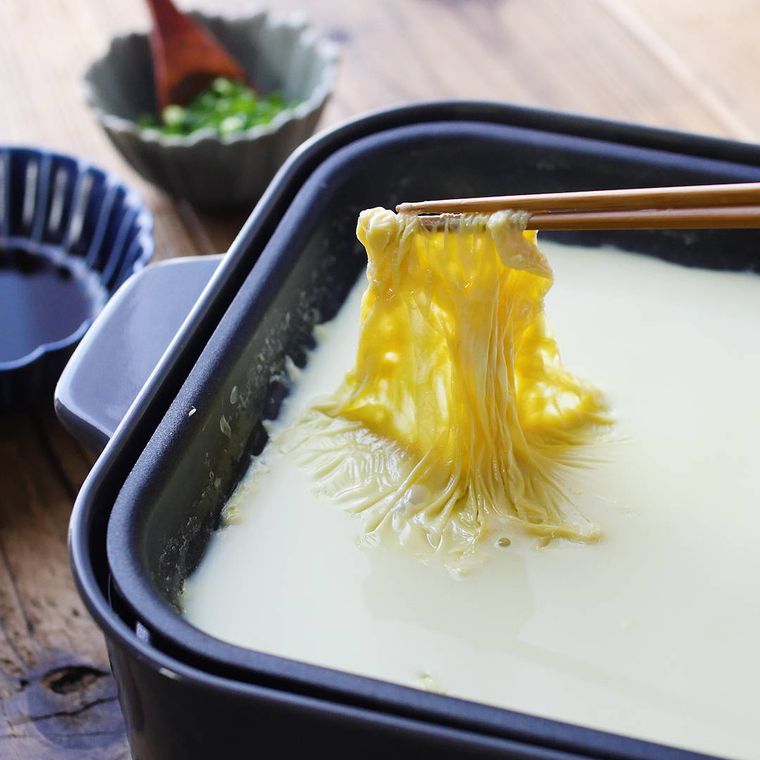 ホットプレートに入った豆乳チーズリゾットのゆばを、箸でつまんでいる様子