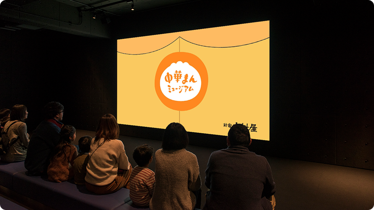 スクリーンに中華まんミュージアムの映像が映し出されている