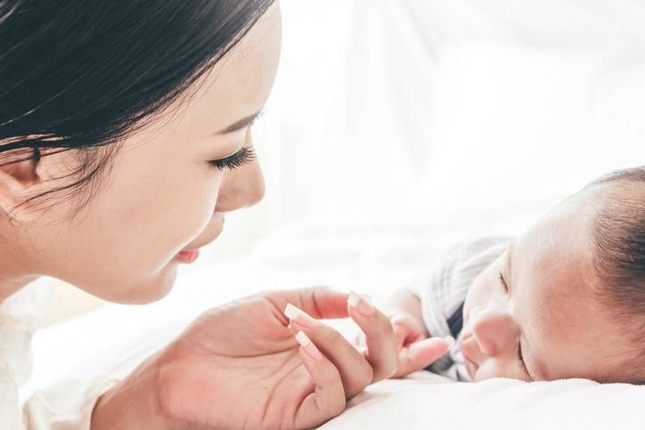 赤ちゃんが母親の指を掴んで寝ている様子