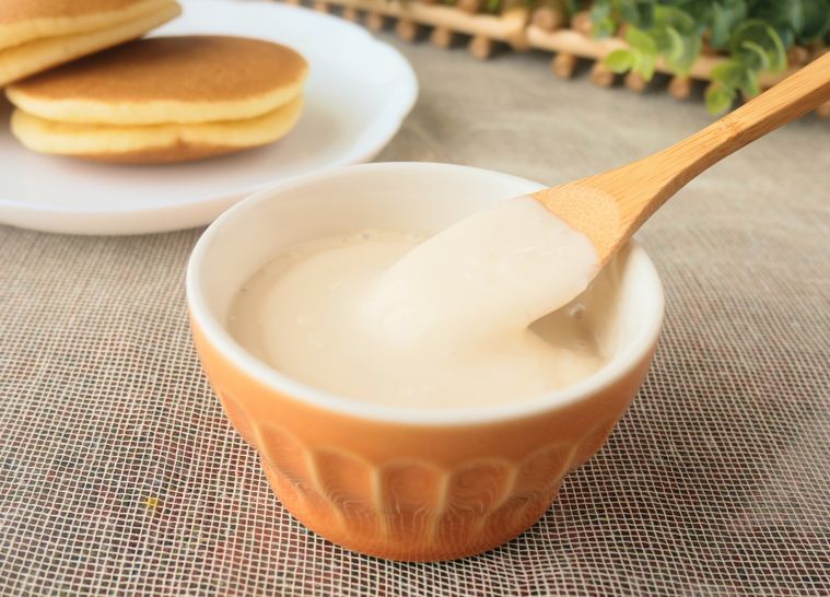 オレンジ色のココットに入った豆乳クリームを、木製のスプーンですくう様子