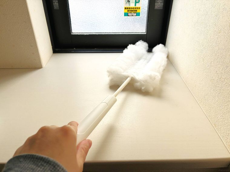 のばしたハンディモップで棚を掃除している