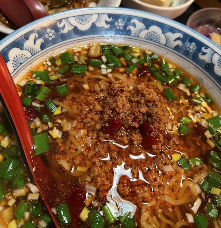 青い柄が入ったどんぶり 赤いレンゲとニラ、台湾ミンチ,刻みネギがのる台湾ラーメン