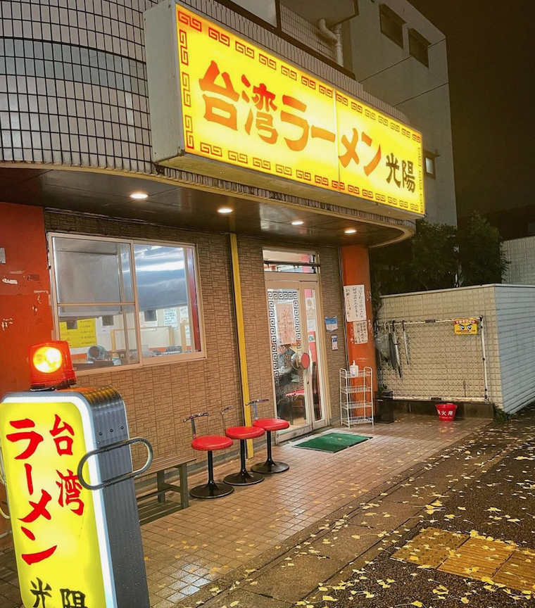 赤文字で屋号が入った黄色い看板 赤い椅子がある外観