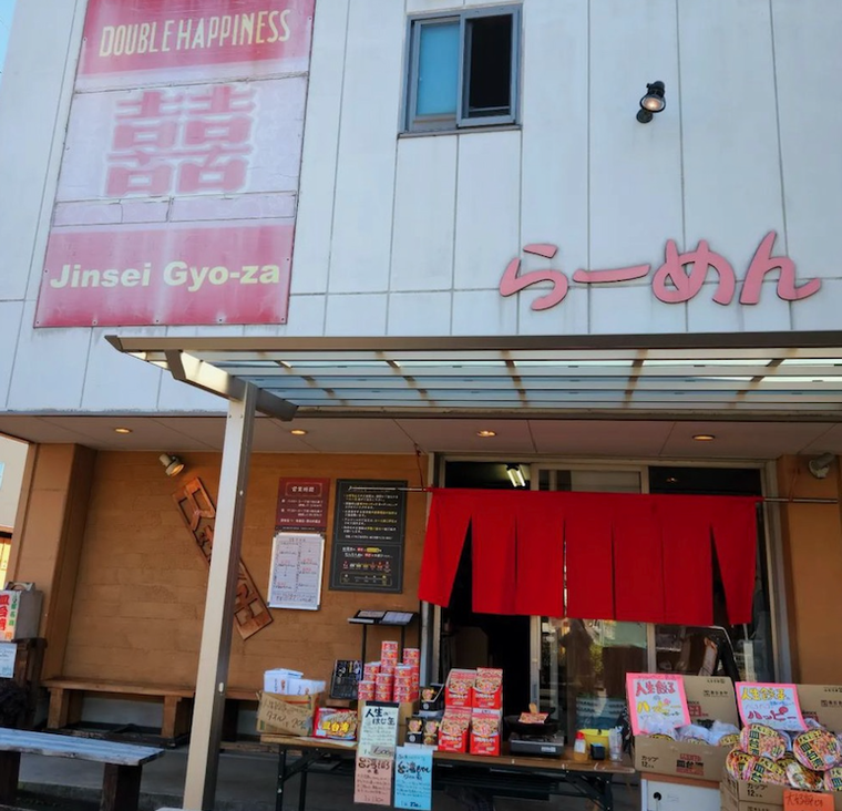赤文字でらーめんと書かれた壁や赤い暖簾、物販が並んだ人生餃子の外観
