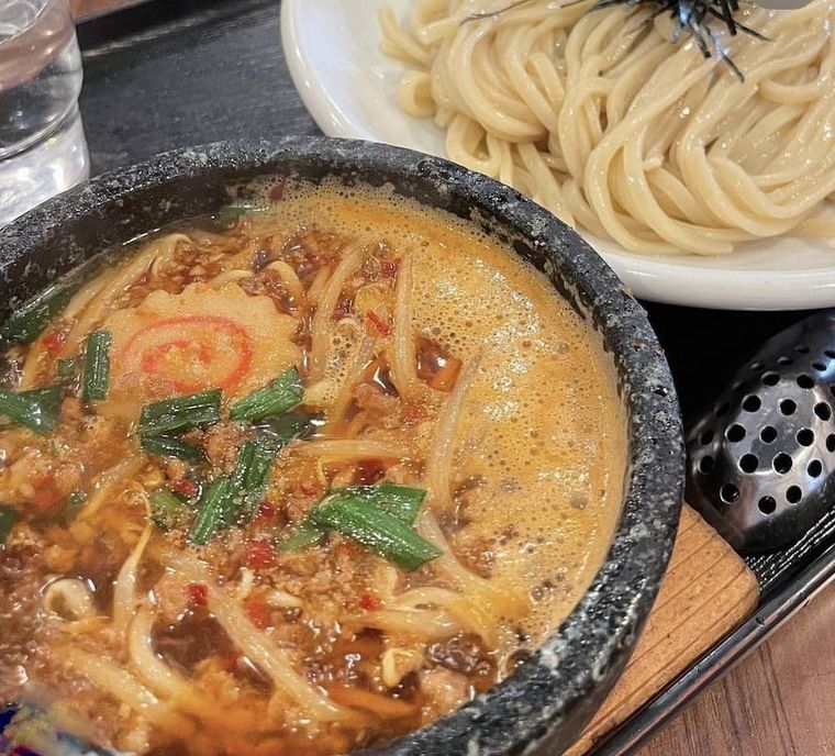 ミンチ、にら、唐辛子、なるとが入った土鍋のつけ汁と白いお皿にのった麺