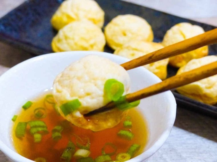 お箸で明石焼きをつまんで、だし汁に浸けた様子