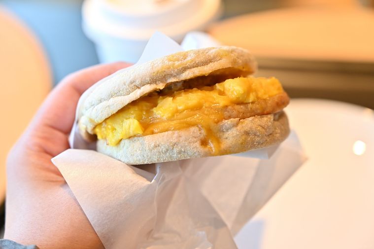 スクランブルエッグやチーズなどをサンドしたイングリッシュマフィンを手に持っている