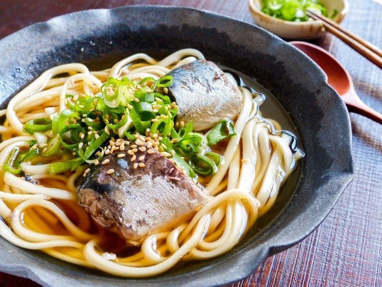 ねぎとごまをトッピングしたさば缶うどんが黒い皿に盛り付けられているところ