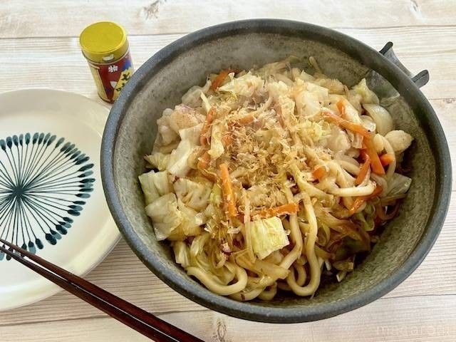 茶色い大皿に入ったホルモン焼きうどんが和風の皿に盛り付けられているところ