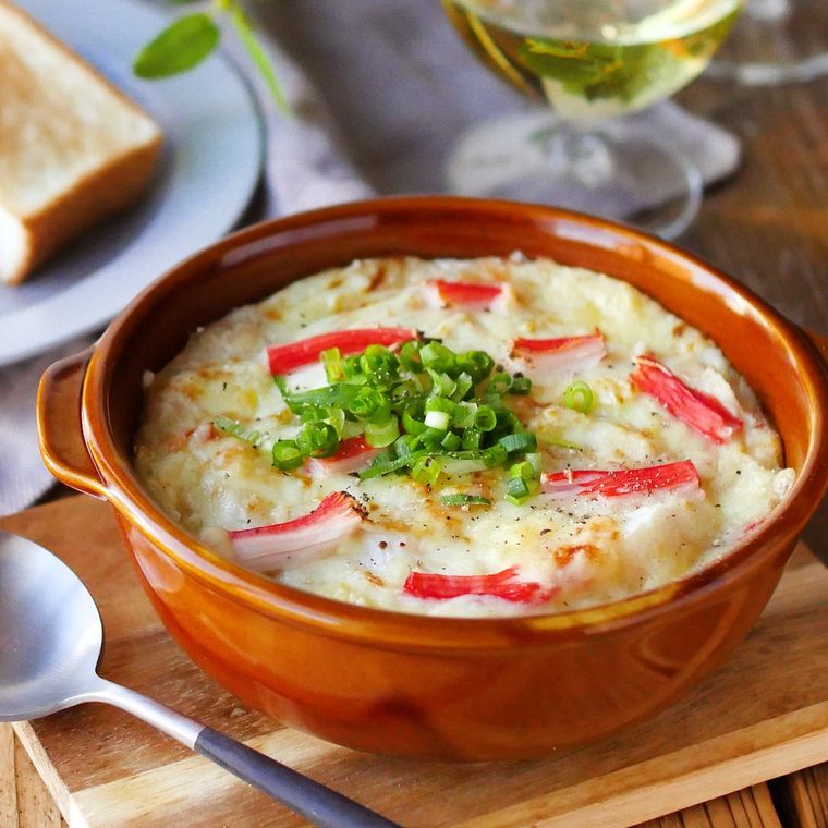 茶色のグラタン皿に盛られ、小口ねぎをトッピングしたカニカマと長芋のみそグラタン