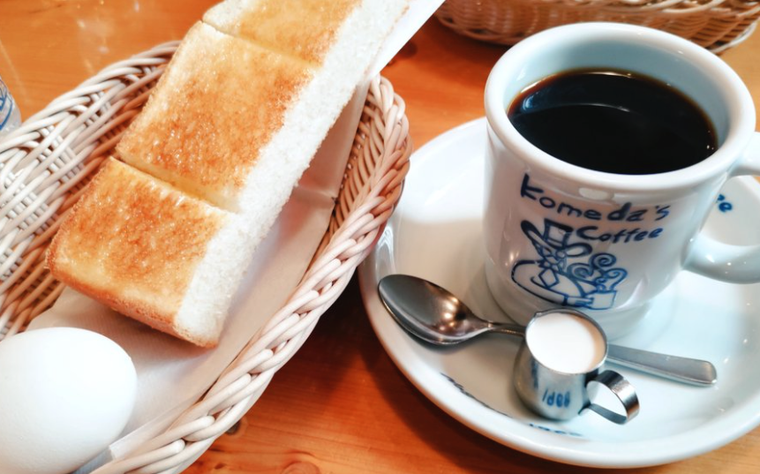 左にかごに入った半分のトースト、右にホットコーヒーとミルクとティースプーン