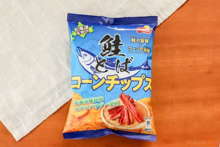 白いランチョンマットを斜めに敷いた木製のテーブルの上に置かれた鮭とばコーンチップス