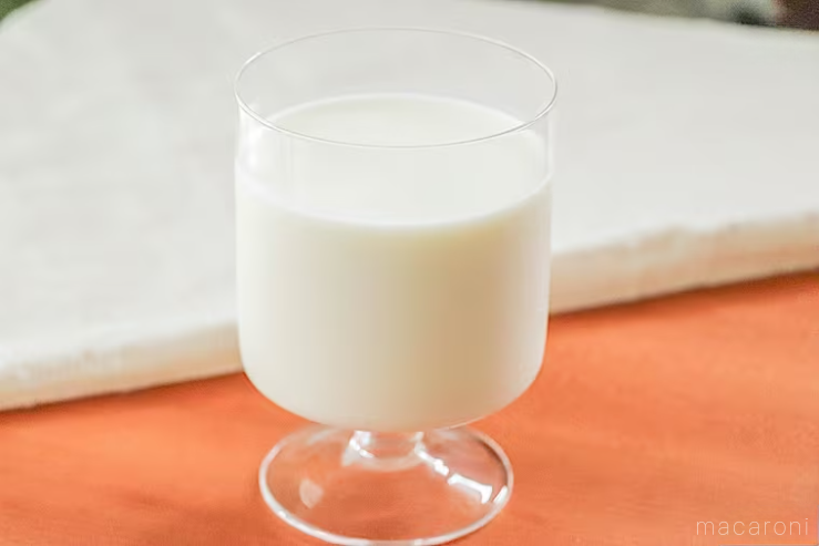 白いランチョンマットを背景にグラスに入った北海道牛乳が木製のテーブルの上に置かれている