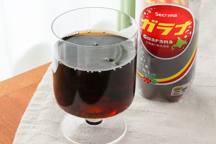 白いランチョンマットの上にガラナを注いだ透明なグラスとペットボトルが置かれている