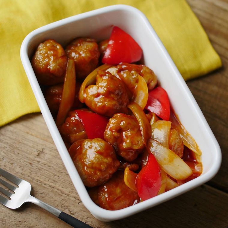 白い保存容器に入っている豚こまボールと赤パプリカの酢豚