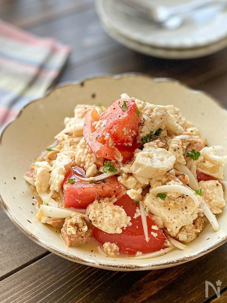 ベージュの皿に盛られた新玉ねぎとトマトのサラダ