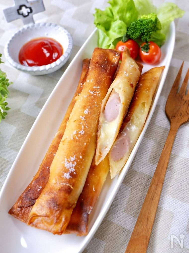 白く細長いお皿にのせられた魚肉ソーセージとチーズのスティック春巻きとサラダ