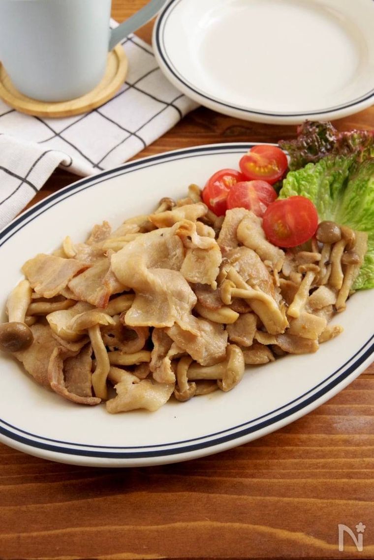 白地に青いラインが入った器に盛られた豚バラとしめじの炒め物とプチトマトとレタス