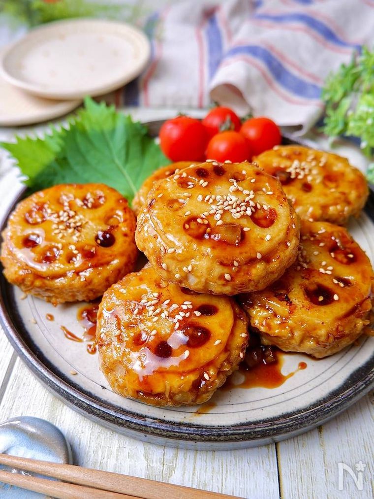 縁が黒い器に盛られた甘酢れんこんつくねバーグと大葉とミニトマト