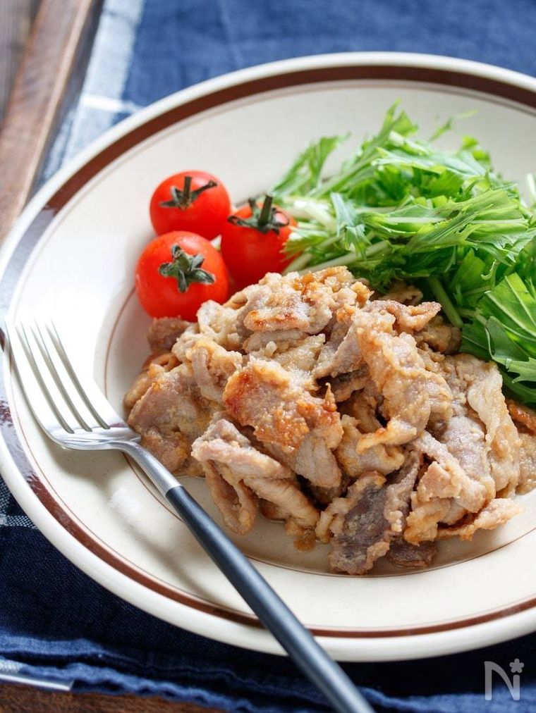 茶色いライン入りの丸皿に豚こまの味噌マヨ漬けとミニトマトと水菜を盛った様子