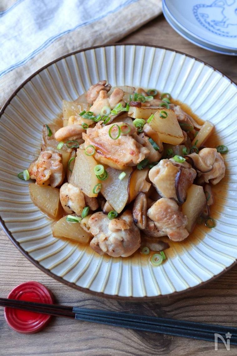 丸い器に盛られた鶏肉と大根としいたけの甘辛煮と黒い箸