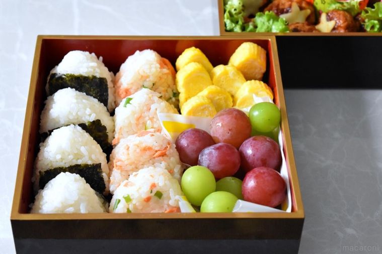 重箱に詰めたおにぎり、フルーツ、だし巻き卵