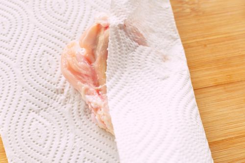 開いた手羽元の水気をキッチンペーパーでふき取る様子