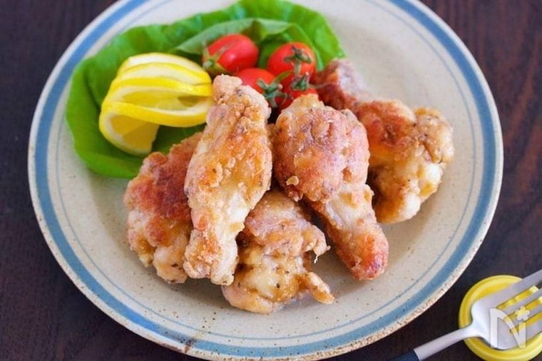 丸い器に盛り付けられた鶏手羽元の和風フライドチキンとミニトマト、レモン、レタス