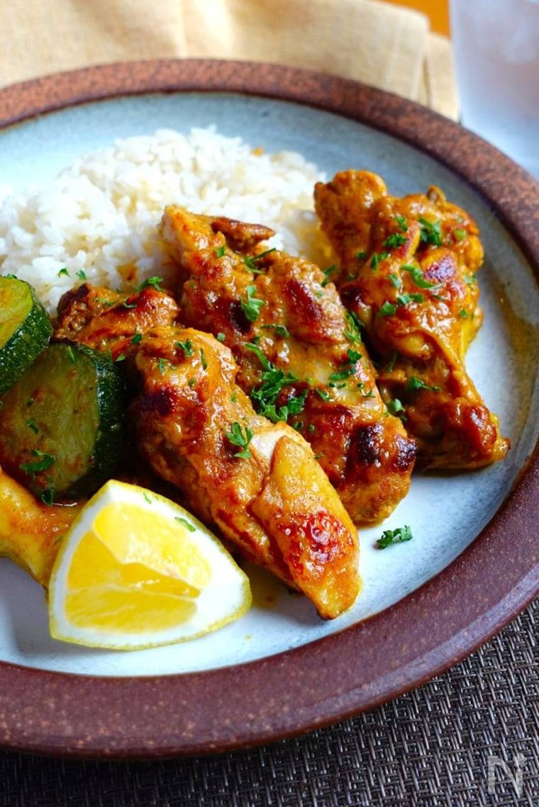 丸い器に鍋られた手羽元のタンドリーチキンとご飯、レモン