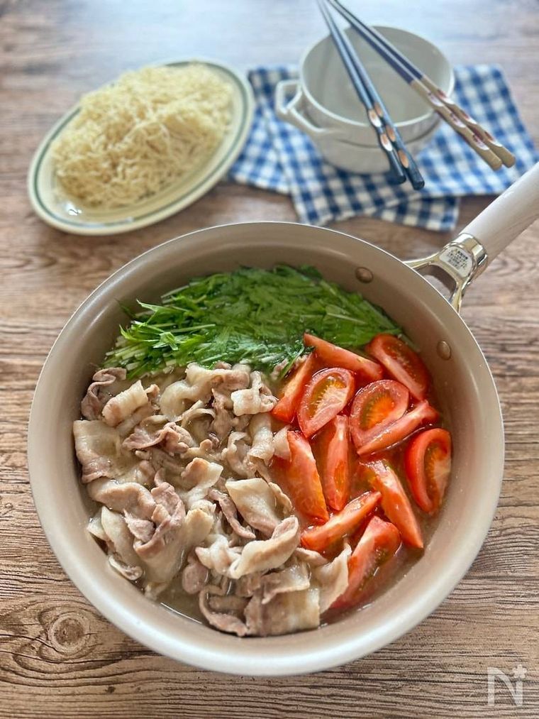 ベージュの鍋に入れられたさっぱりトマトの豚バラ焼肉鍋と2人分の箸、取り皿