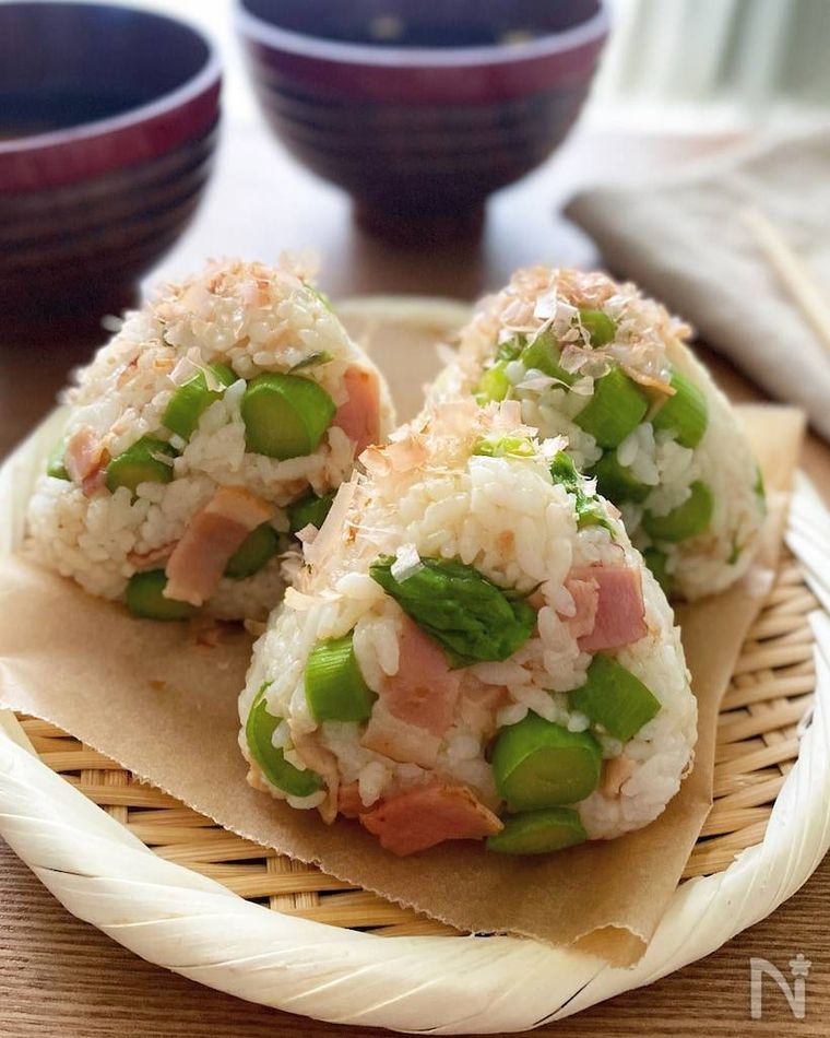 竹ざるに並べられた3個のアスパラベーコンのおにぎり